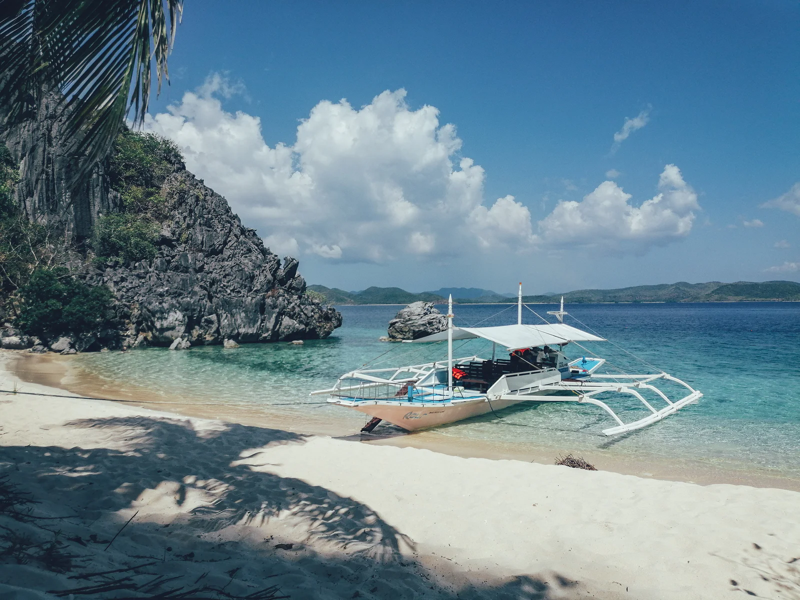 A banca boat moored off the white-sand beach and limestone cliffs of Black Island (Malajon), Busuanga.